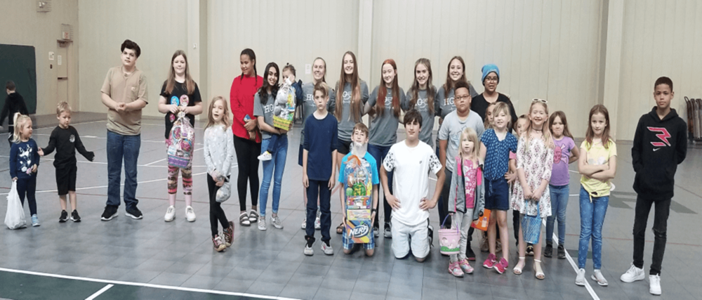 A group of children and volunteers smiling on a gym floor