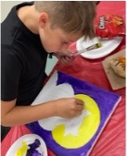 A young boy is focused intently on painting a moon behind a cat.