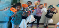 4 children are standing by a door while they hold up the paper monsters that they hand made. 