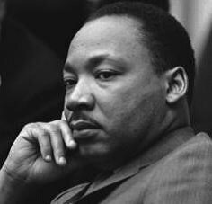 Martin Luther King, Jr. looks off into the distance while resting his head in his hand.