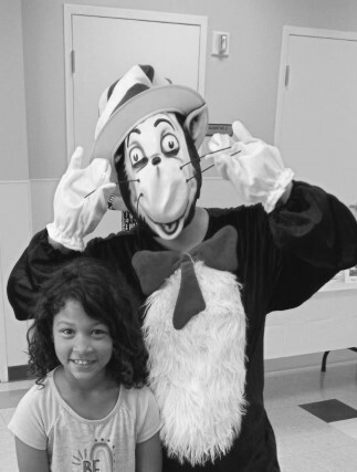 A girl standing with a person in a cat in the hat costume.