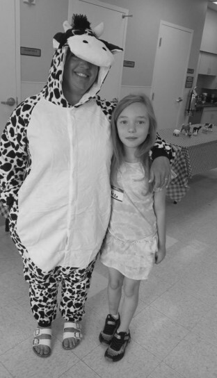 A girl wearing a dress standing with a woman in a cow costume.